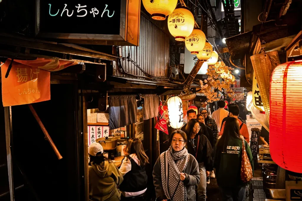 Omoide Yokocho de nuit à Tokyo et ses izakayas traditionnels Ruelle animée d’Omoide Yokocho à Tokyo avec lanternes japonaises, petits restaurants izakaya et passants dans une ambiance nocturne typique du Japon.