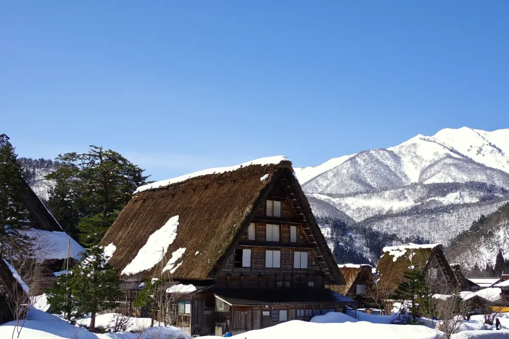 Maisons traditionnelles de Shirakawa-go sous la neige en hiver Village traditionnel de Shirakawa-go au Japon en hiver avec maisons japonaises aux toits de chaume recouverts de neige et montagnes enneigées en arrière-plan.