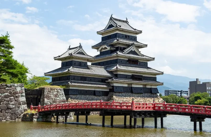 Château de Matsumoto dans les Alpes japonaises Château de Matsumoto avec pont rouge et montagnes en arrière-plan.