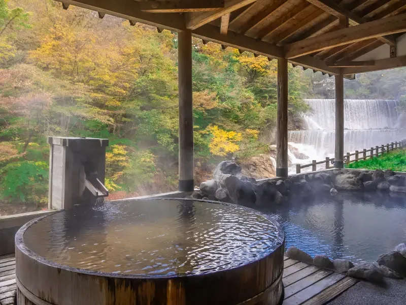 Onsen traditionnel au Japon – Détente au cœur de paysages d’exception Onsen extérieur japonais avec vue sur la nature et cascade dans un ryokan traditionnel