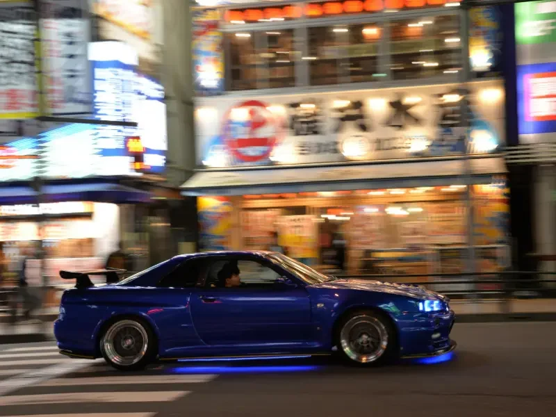 Immersion dans la culture JDM à Tokyo – Entre passion et sensations Voiture sportive japonaise roulant de nuit dans une rue animée de Tokyo