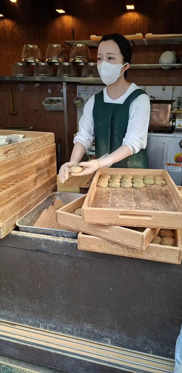 Préparation de mochi, spécialités culinaires traditionnelles à Nara Artisane japonaise préparant des mochis traditionnels dans une boutique de Nara au Japon, avec plateaux en bois.