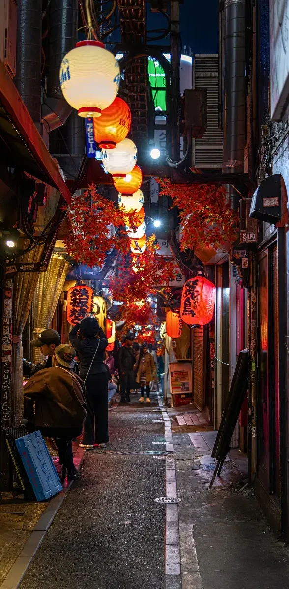 Ruelle illuminée d’Omoide Yokocho à Tokyo entre lanternes japonaises et petits restaurants traditionnels la nuit Petite ruelle animée d’Omoide Yokocho à Tokyo, bordée de lanternes japonaises rouges, d’izakaya traditionnels et de street food.