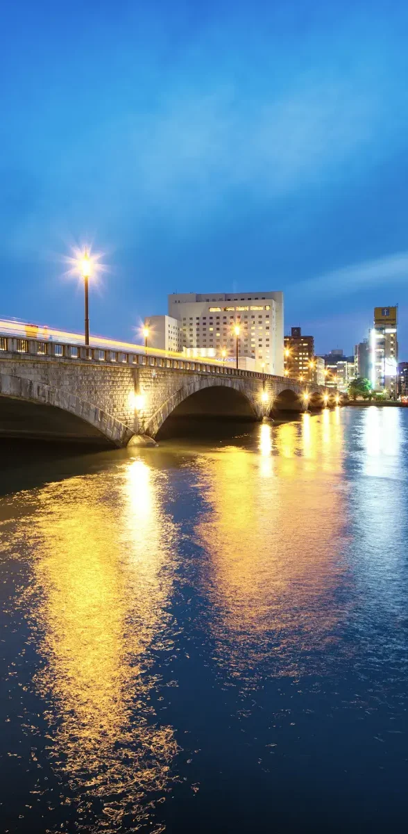 Ville de Niigata la nuit avec pont éclairé et reflets sur l’eau au Japon