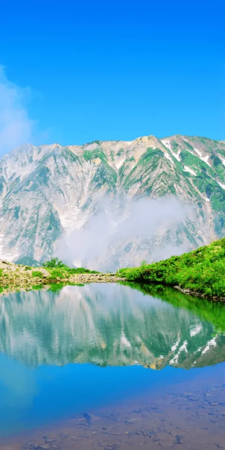 Lac de montagne aux eaux calmes reflétant les Alpes japonaises sous un ciel bleu, illustrant le Pack Ajisai au Japon.