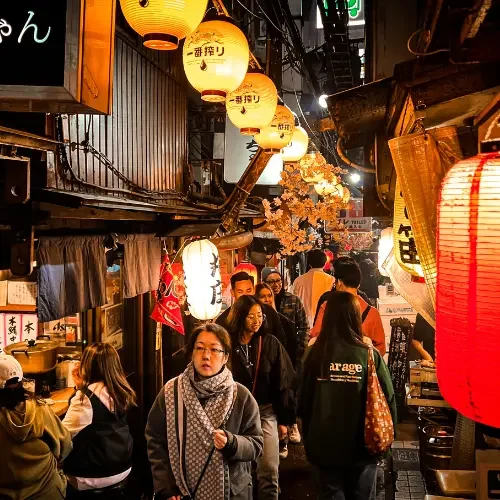 Ruelle japonaise bordée d'izakayas éclairés par des lanternes, animée par les habitants et voyageurs