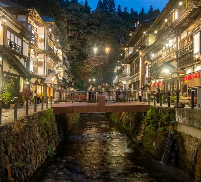 Ruelle de Ginzan Onsen bordée de ryokan traditionnels illuminés au bord de la rivière.