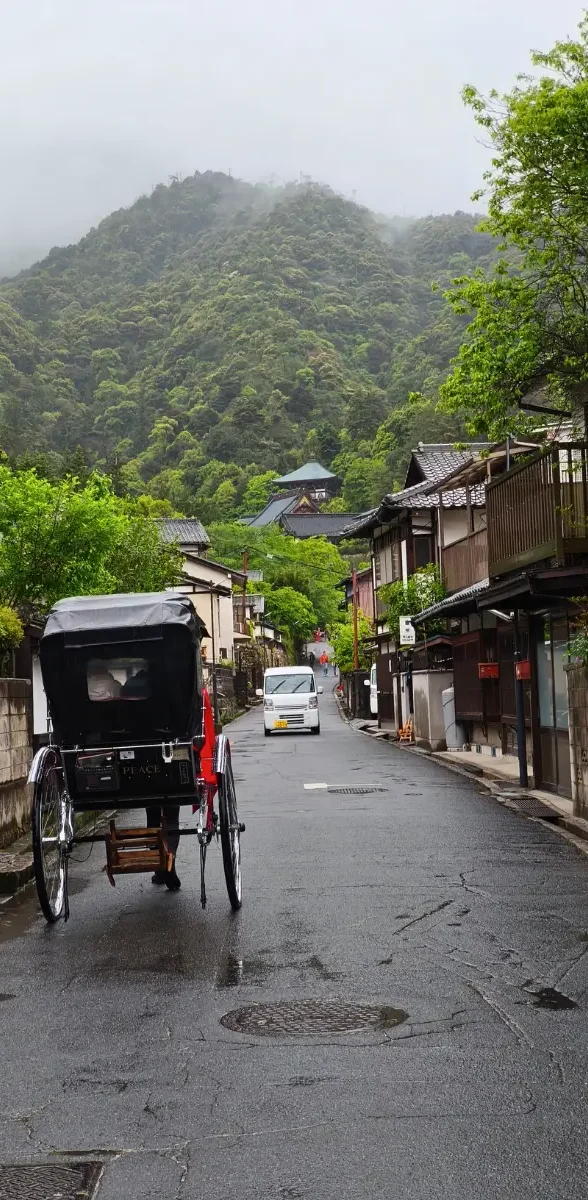 Rue paisible de Miyajima sous la pluie avec un pousse-pousse traditionnel et des montagnes verdoyantes en arrière-plan à Hiroshima, au Japon