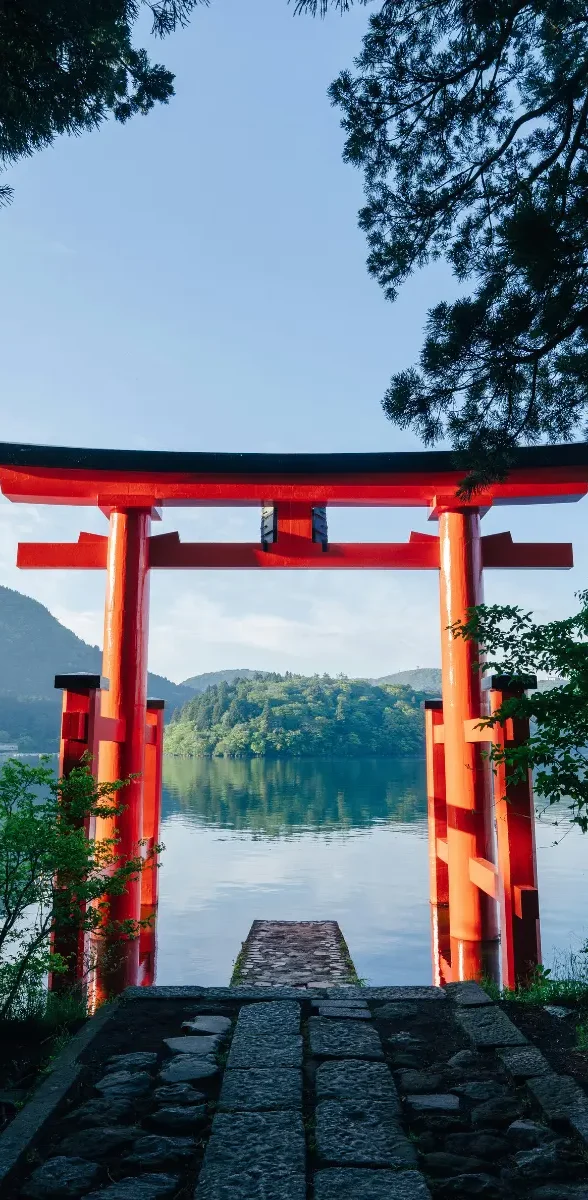 Torii rouge au bord du lac Ashi à Hakone entouré de forêt au Japon