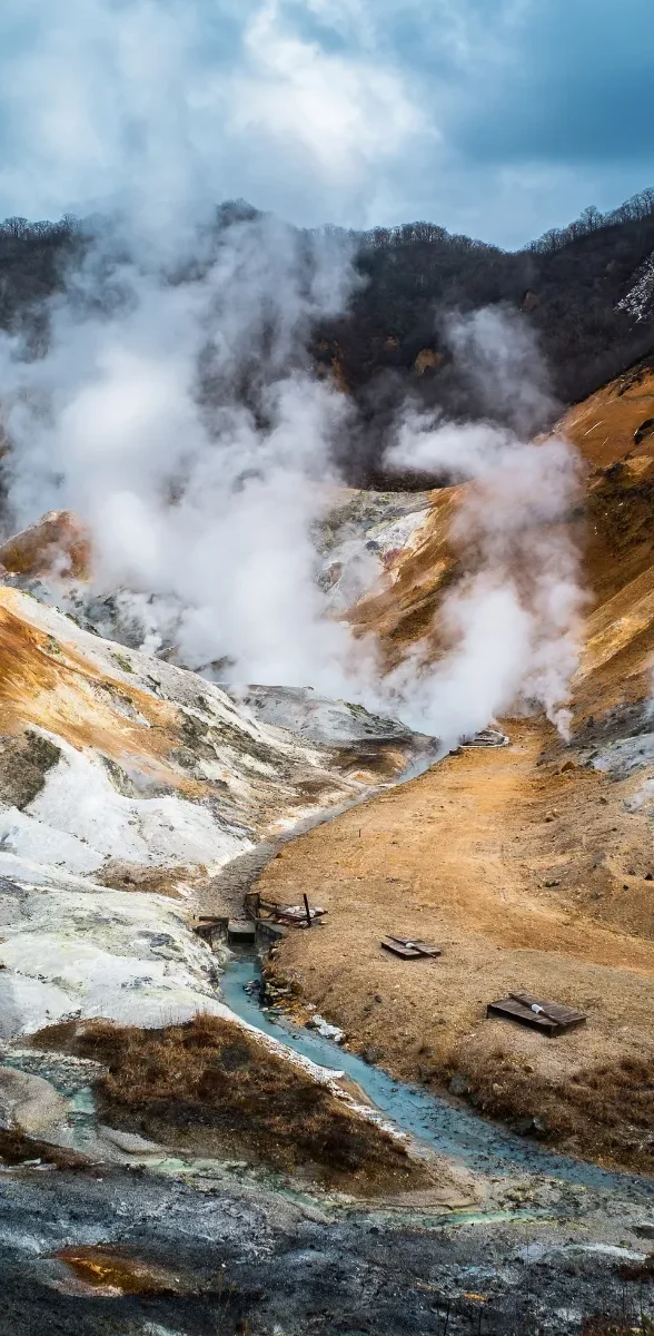 Vallée volcanique de Noboribetsu à Hokkaido Paysage volcanique de Jigokudani à Noboribetsu, à Hokkaido, avec vapeur géothermique, reliefs minéraux et sentier traversant la vallée.