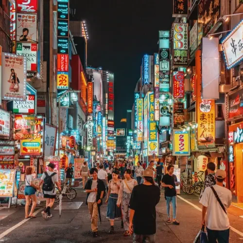 Rue animée de Tokyo de nuit avec enseignes lumineuses et foule dans un quartier emblématique du Japon