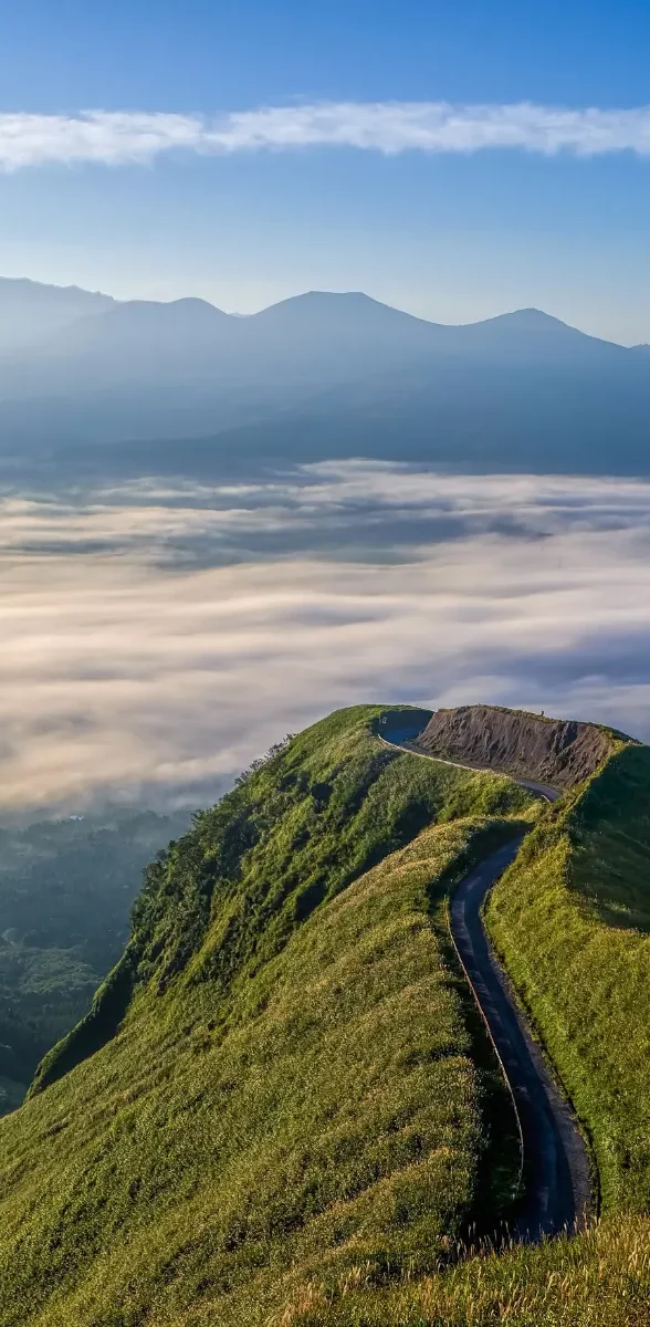 Route panoramique sur les hauteurs du Mont Aso à Kumamoto, avec collines verdoyantes et mer de nuages au Japon.