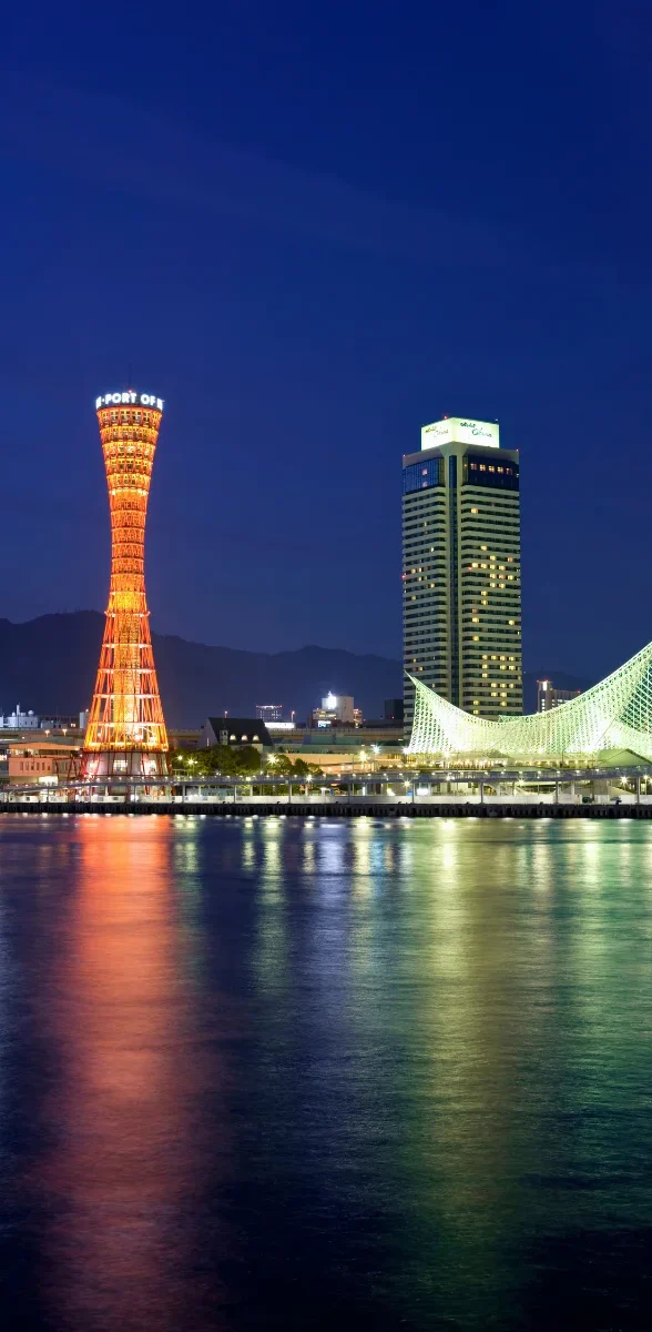 Vue nocturne du port de Kobe dans la préfecture de Hyogo, avec la Kobe Port Tower illuminée et les reflets de la ville sur l’eau.