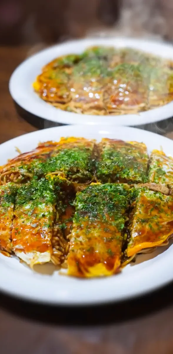 Okonomiyaki traditionnel d’Hiroshima servi chaud sur une assiette, garni de sauce japonaise et d’algues séchées au Japon.