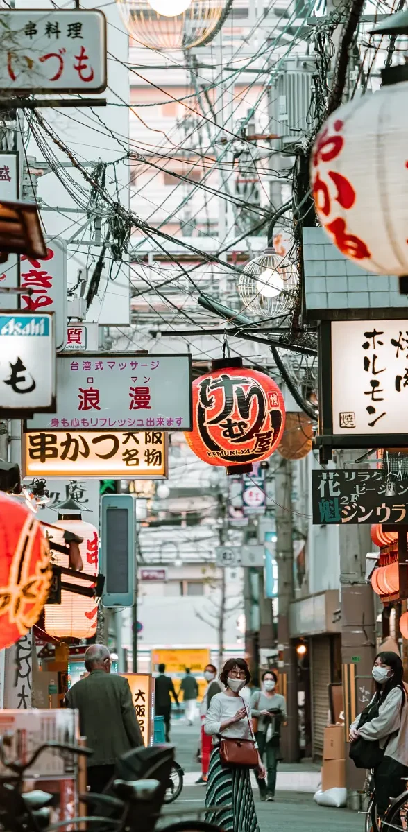 Ruelle commerçante typique et street food à Osaka au Japon Petite rue animée d’Osaka avec lanternes japonaises, enseignes lumineuses, restaurants locaux et ambiance typique des street markets