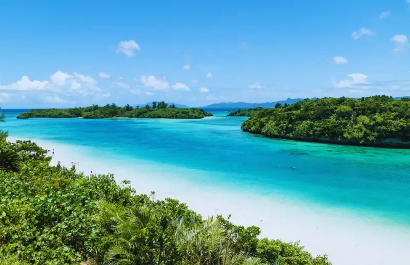 Voyage Japon 15 jours – Itinéraire Himawari | J'Go Japon Plage de sable blanc bordée d'eaux turquoise et d'une végétation luxuriante.
