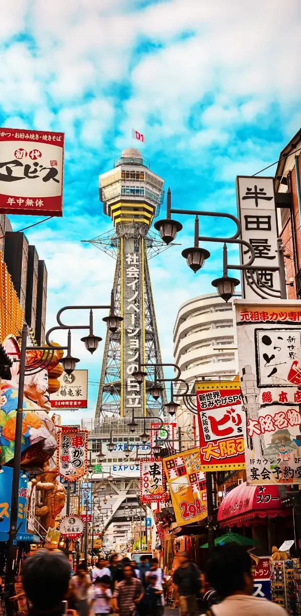Tour Tsūtenkaku et ambiance animée du quartier Shinsekai à Osaka Vue de la tour Tsūtenkaku au cœur du quartier Shinsekai à Osaka, entourée d’enseignes japonaises, restaurants et rues animées typiques.