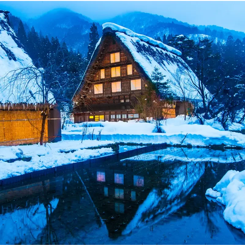 Village traditionnel de Shirakawa-go sous la neige au Japon Maison traditionnelle enneigée à Shirakawa-go au Japon avec reflet dans l’eau – paysage hivernal