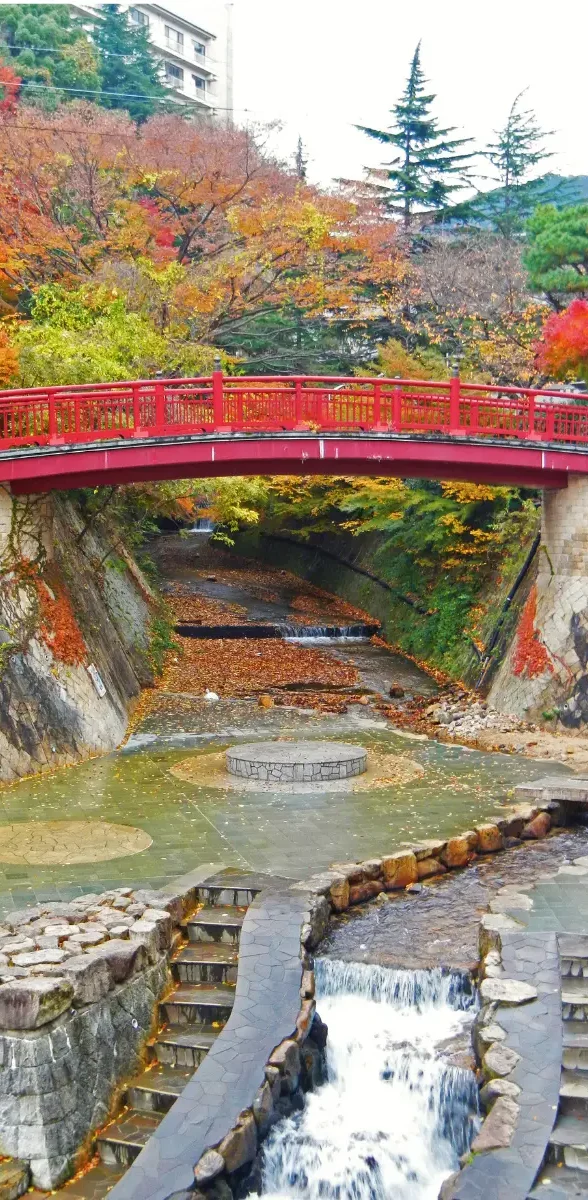 Pont rouge traversant la rivière d’Arima Onsen dans la préfecture de Hyogo, entouré de paysages automnaux.