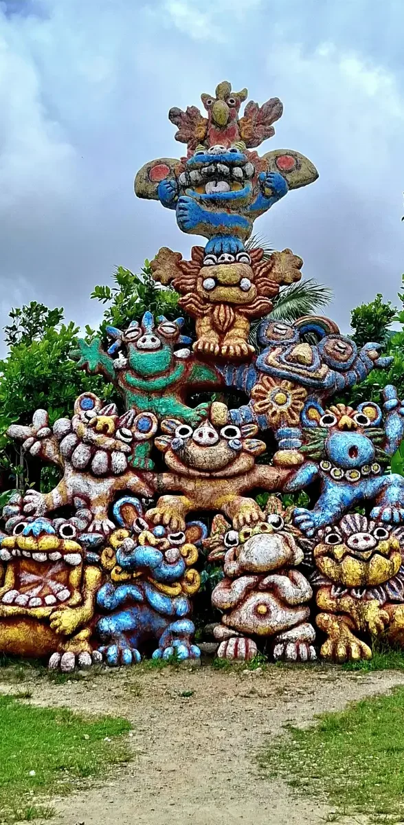 Grande statue artistique colorée dans un parc tropical à Ishigaki, sur l’île d’Okinawa au Japon, avec montagnes verdoyantes en arrière-plan.