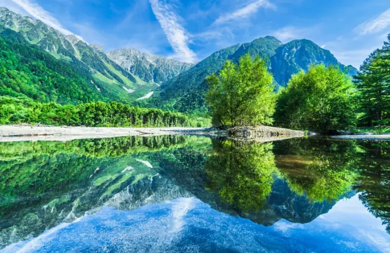 Voyage Japon 15 jours – Itinéraire Ajisai | J'Go Japon Rivière paisible entourée de montagnes et d'arbres reflétés dans l'eau claire.