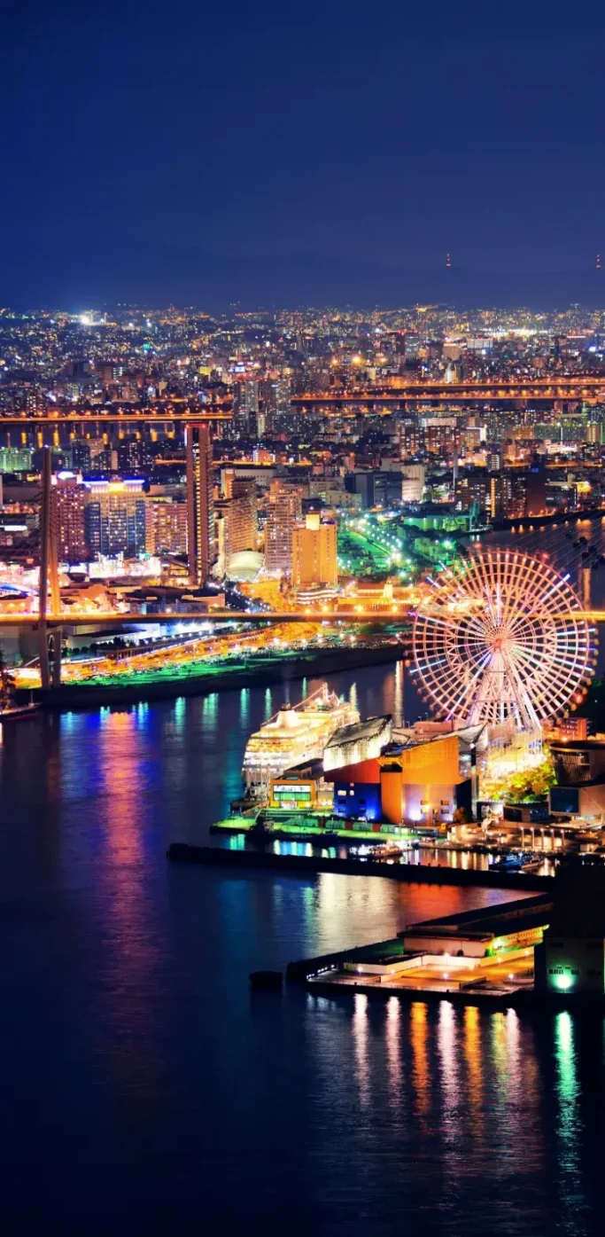 Baie d’Osaka de nuit avec grande roue et skyline illuminée Vue nocturne de la baie d’Osaka avec grande roue et bâtiments illuminés au Japon